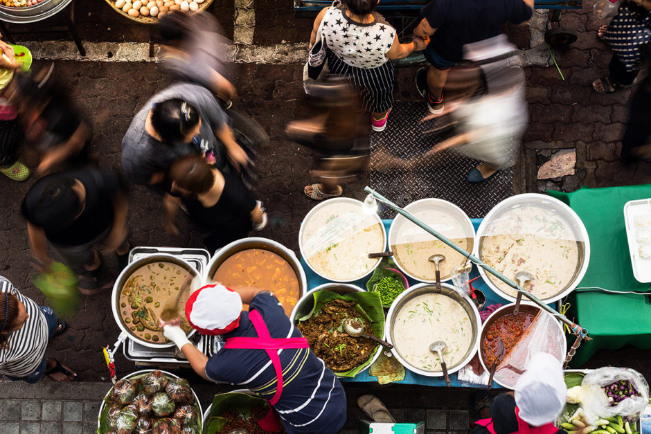 A view from above of a city street food vendor preparing food with people walking past